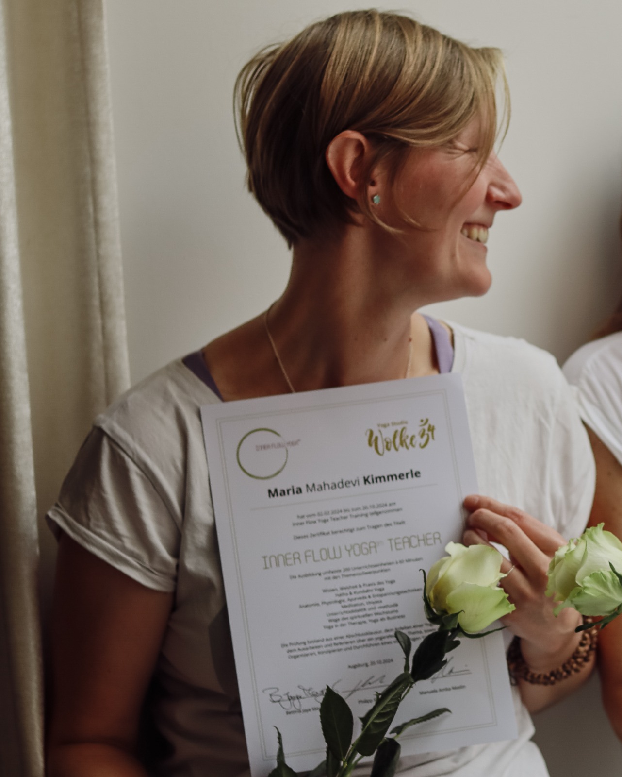 Bild von der lachenden Maria auf dem sie ihr Zertifikat asl Yoga Lehrer hält. Daruf steht ihr Yoga-Name Maria Mahadevi Kimmerle.